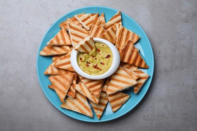 Photo of Delicious pita chips with hummus on grey table, top view