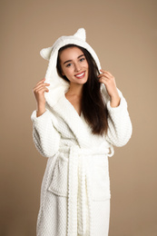 Photo of Beautiful young woman in bathrobe with funny hood on brown background