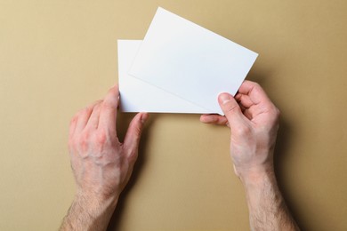 Man holding flyers on light brown background, top view. Mockup for design