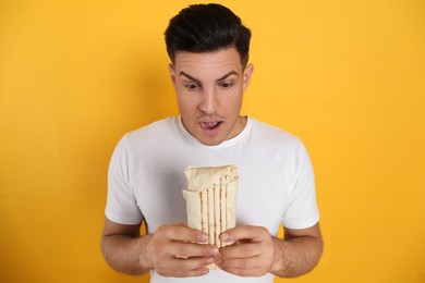 Emotional man with delicious shawarma on yellow background