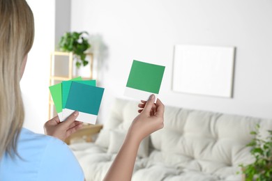 Photo of Woman choosing paint shade for wall in room, focus on hands with color sample cards. Interior design
