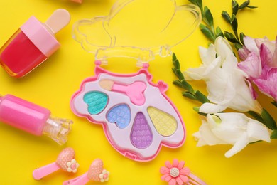 Photo of Decorative cosmetics for kids. Eye shadow palette, lipsticks, accessories and flowers on yellow background, flat lay