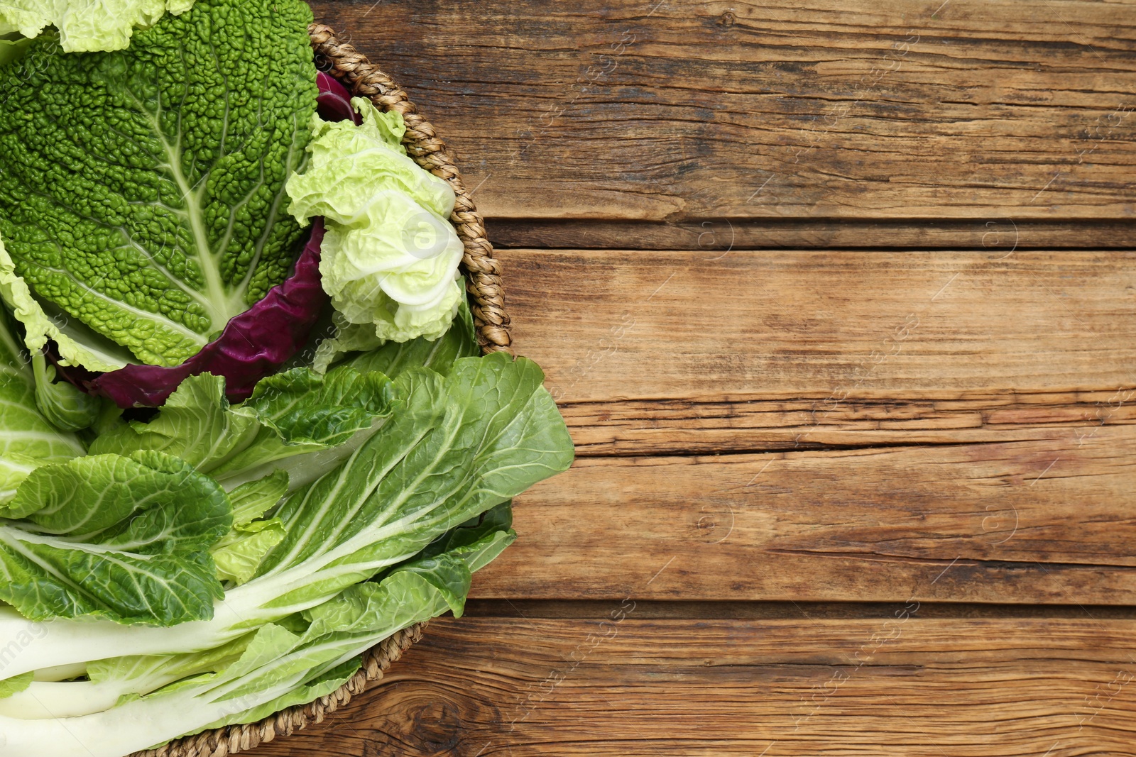 Photo of Many different cabbage leaves on wooden table, top view. Space for text