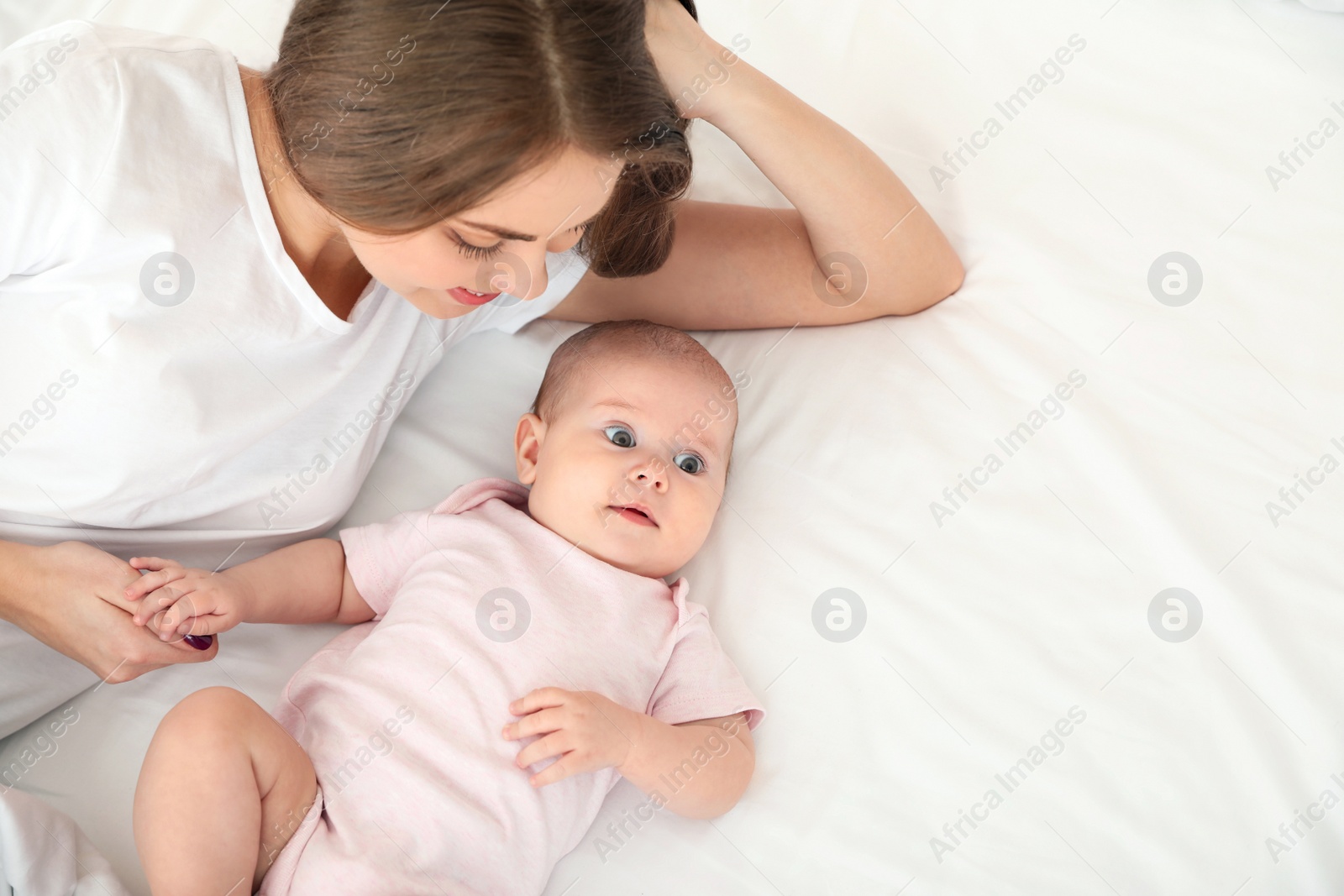 Photo of Cute baby with mother lying on bed, above view. Space for text