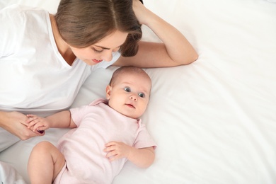 Cute baby with mother lying on bed, above view. Space for text