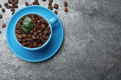 Photo of Cup with roasted coffee beans and leaves on grey table, flat lay. Space for text