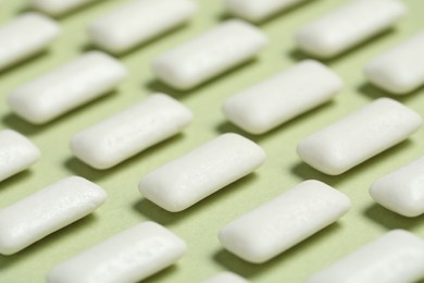 Photo of Tasty white chewing gums on light green background, closeup