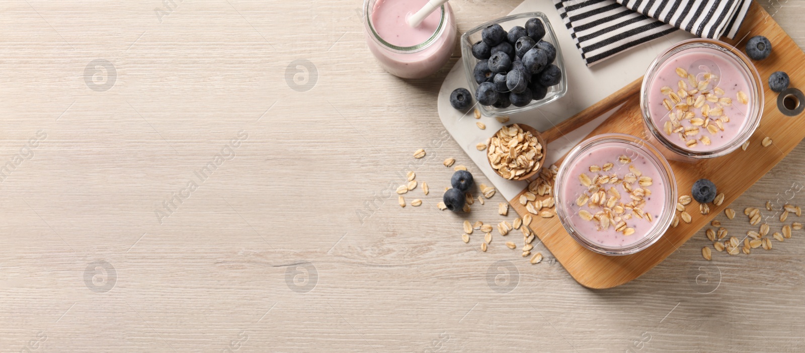 Image of Glasses of tasty blueberry smoothie with oatmeal on wooden table, flat lay with space for text. Banner design