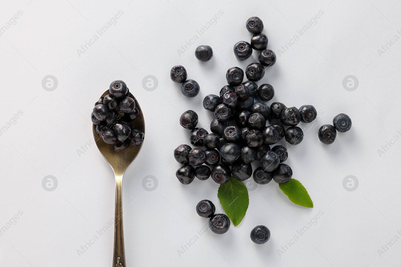 Photo of Spoon with ripe bilberries and leaves on white background, flat lay