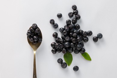 Spoon with ripe bilberries and leaves on white background, flat lay