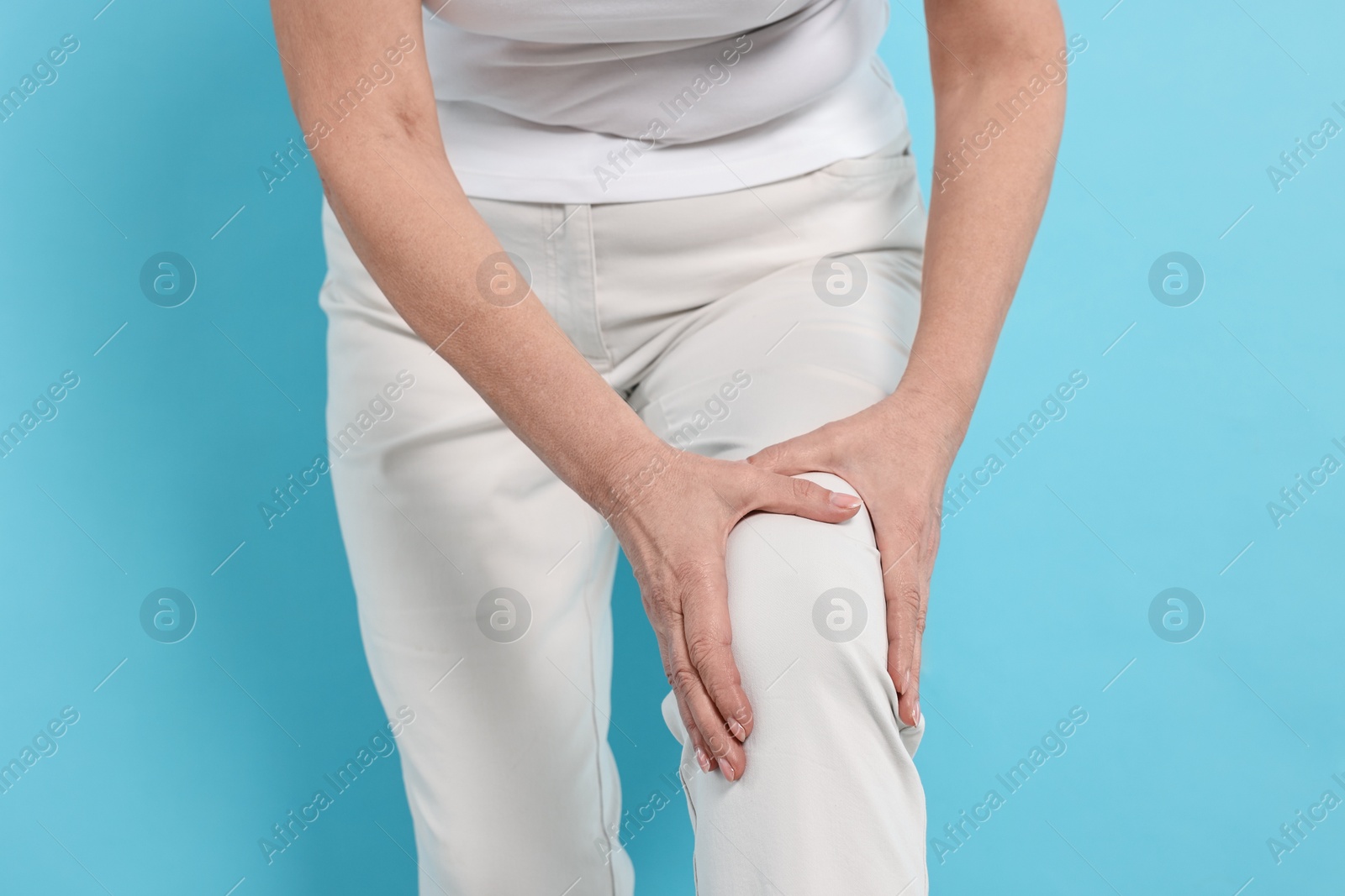 Photo of Arthritis symptoms. Woman suffering from pain in knee on light blue background, closeup