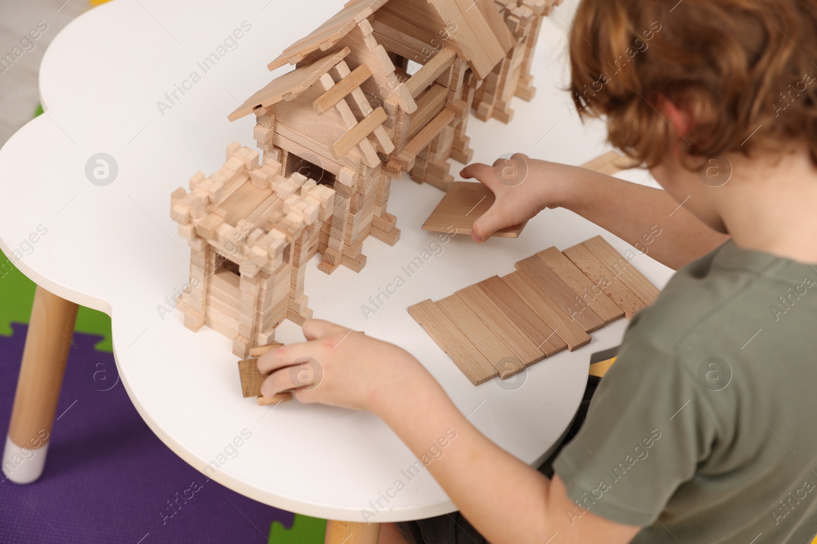 Photo of Little boy playing with wooden entry gate at white table in room, closeup. Child's toy