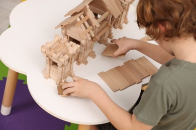 Photo of Little boy playing with wooden entry gate at white table in room, closeup. Child's toy