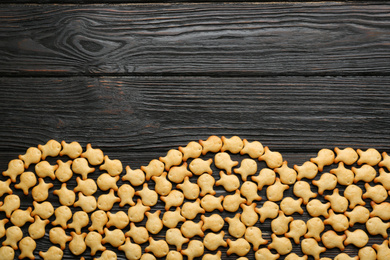 Photo of Delicious fish shaped crackers on black wooden table, flat lay. Space for text