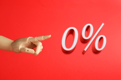 Image of Wooden mannequin hand pointing at sign of zero percent on red background. Special promotion