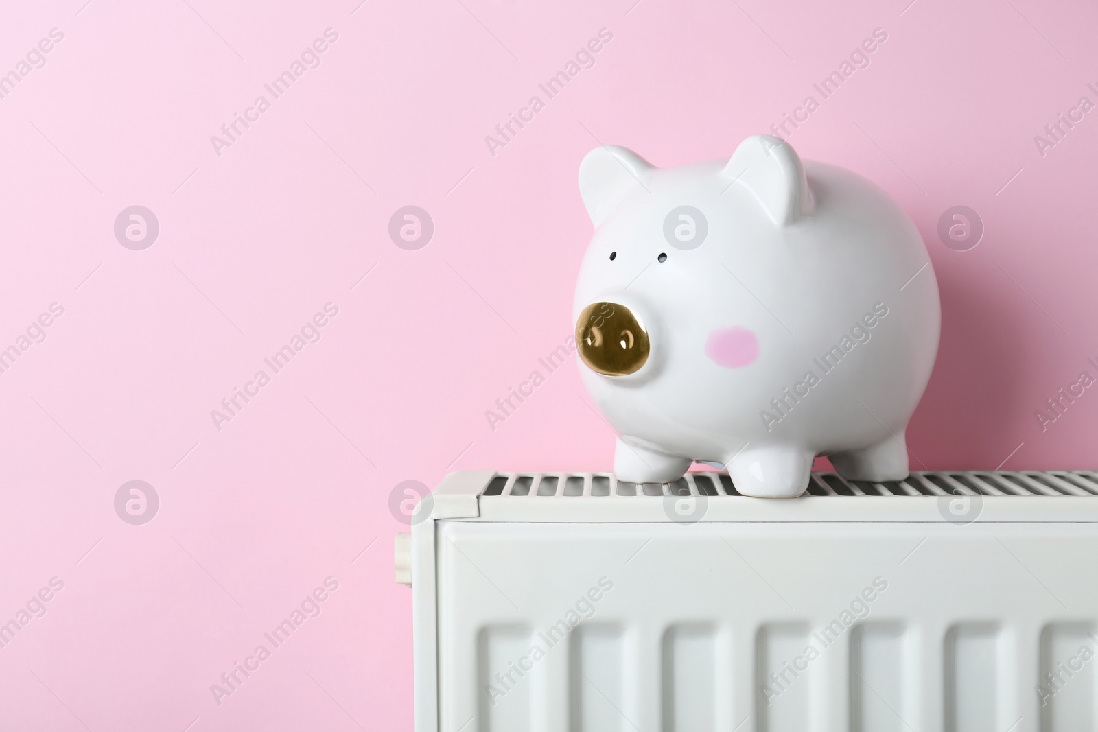 Photo of Piggy bank on heating radiator against pink background, space for text