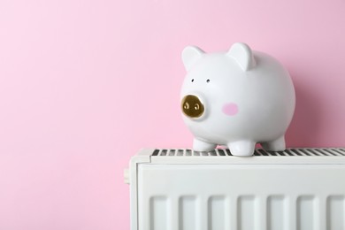 Piggy bank on heating radiator against pink background, space for text