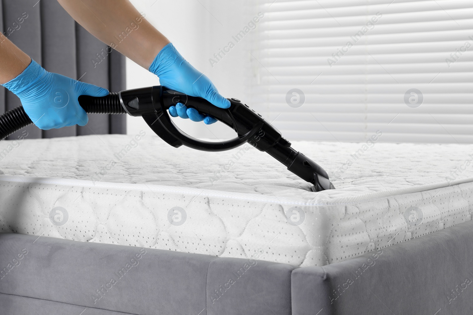 Photo of Woman disinfecting mattress with vacuum cleaner indoors, closeup