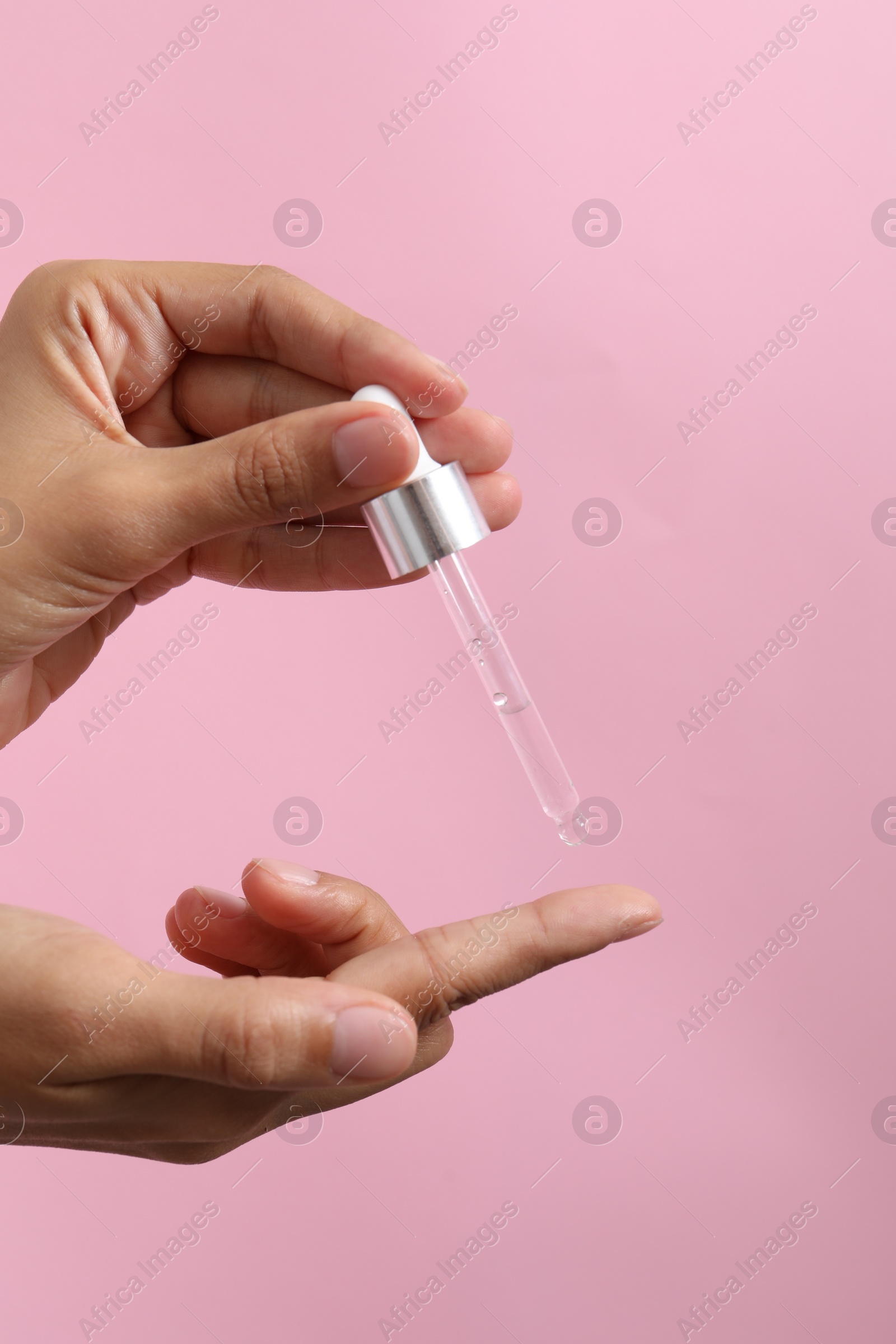 Photo of Woman applying cosmetic serum onto her finger on pink background, closeup