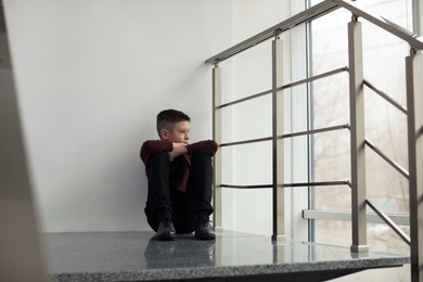 Upset preteen boy sitting on staircase indoors