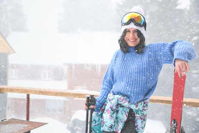 Photo of Young woman with skis wearing winter sport clothes and goggles outdoors