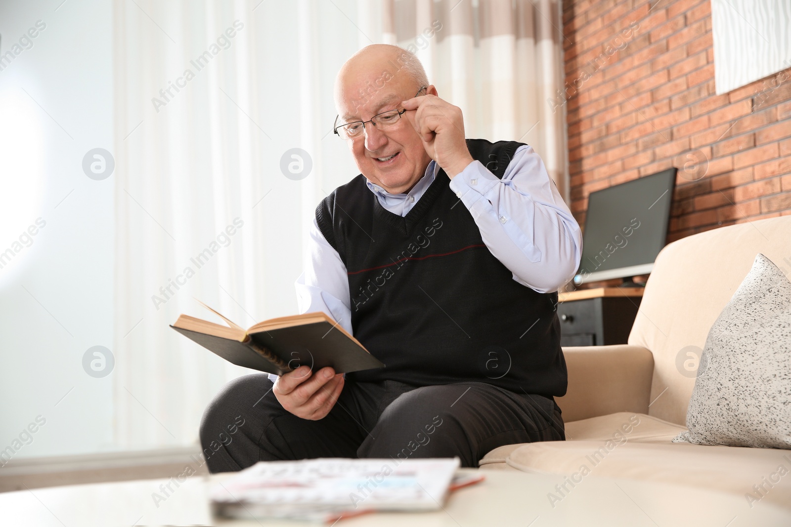 Photo of Elderly man reading book on sofa in living room