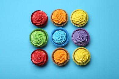 Photo of Many tasty cupcakes with bright cream on light blue background, flat lay