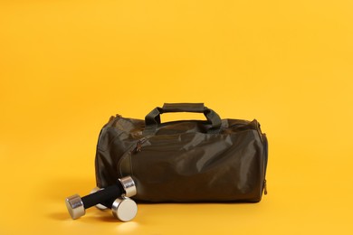 Sports bag and dumbbells on yellow background