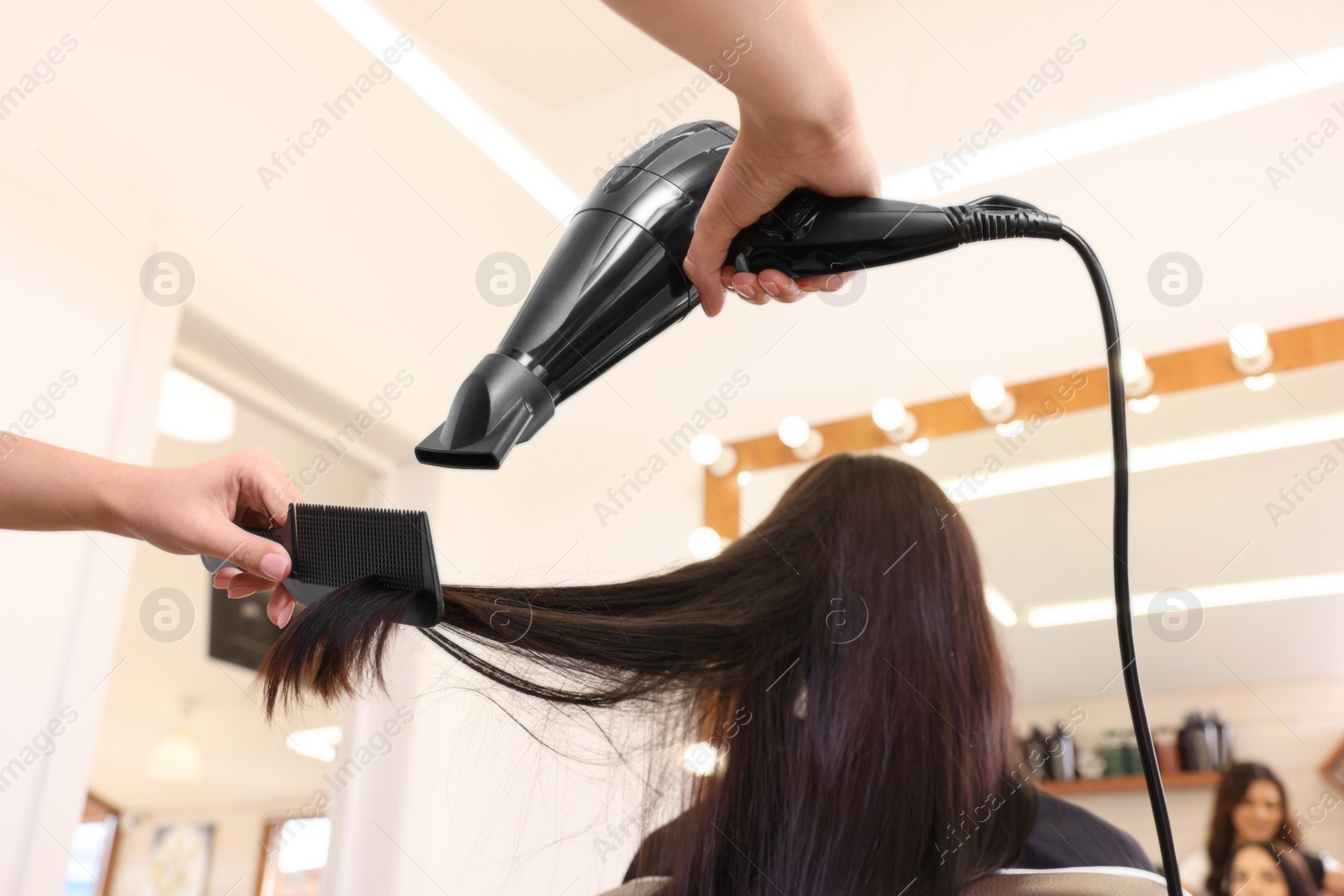 Photo of Hairdresser drying woman's hair in beauty salon, closeup