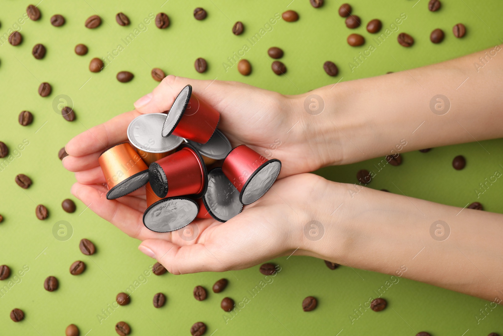 Photo of Woman holding heap of coffee capsules over beans on green background, top view