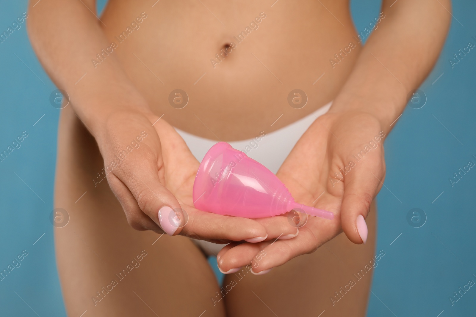 Photo of Woman in white panties with menstrual cup on light blue background, closeup