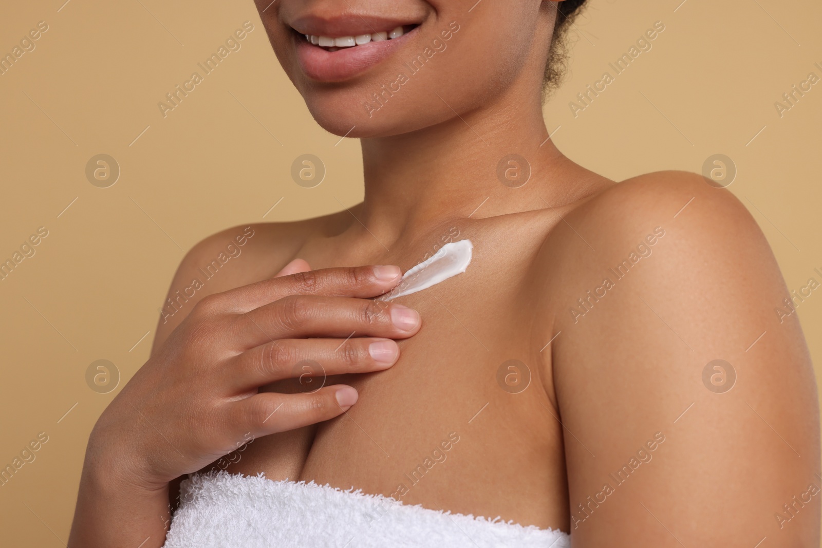 Photo of Young woman applying cream onto body on beige background, closeup