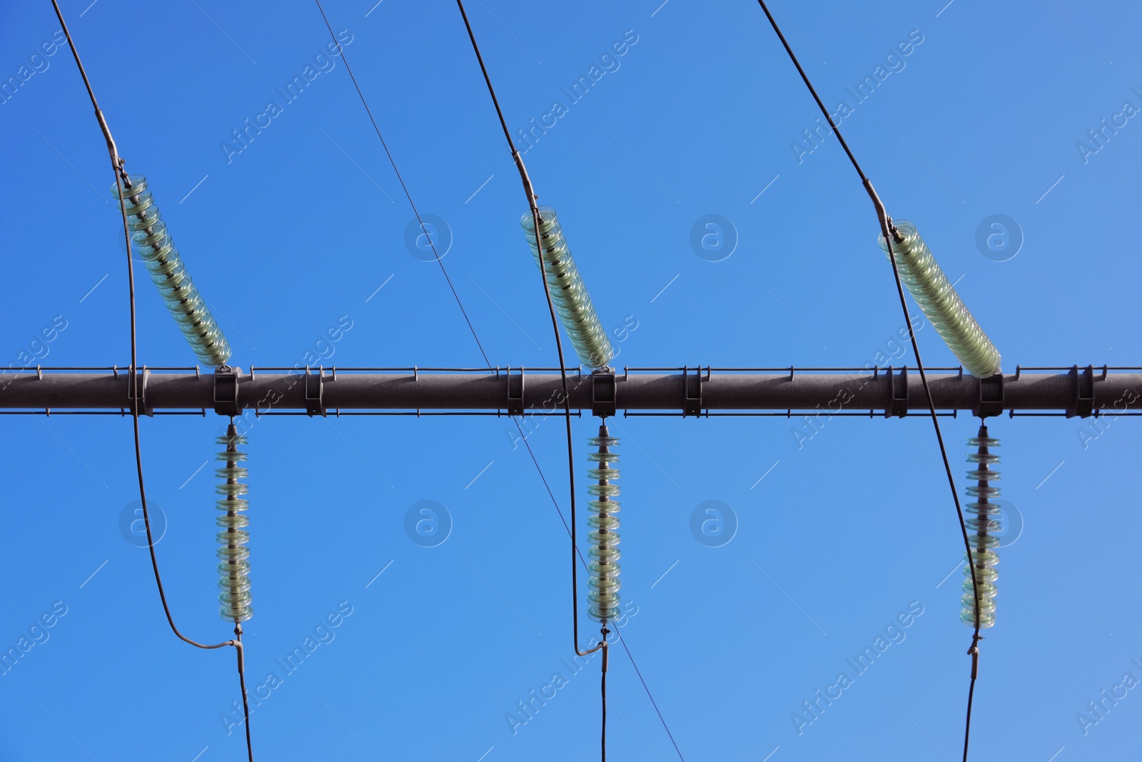 Photo of Electricity transmission power lines against blue sky, low angle view