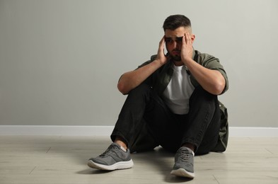 Photo of Sad man sitting on floor near light grey wall. Space for text