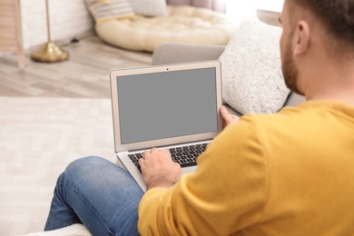 Photo of Young man using video chat on laptop in living room, closeup. Space for design