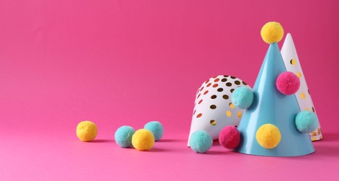 Photo of Party hats with color pompoms on pink background, space for text