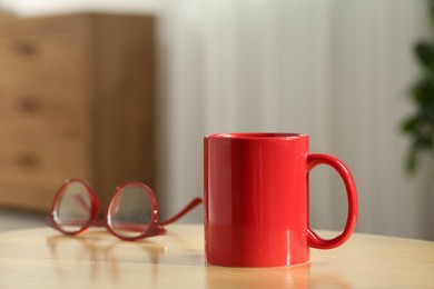 Photo of Red mug and glasses on wooden table indoors. Mockup for design