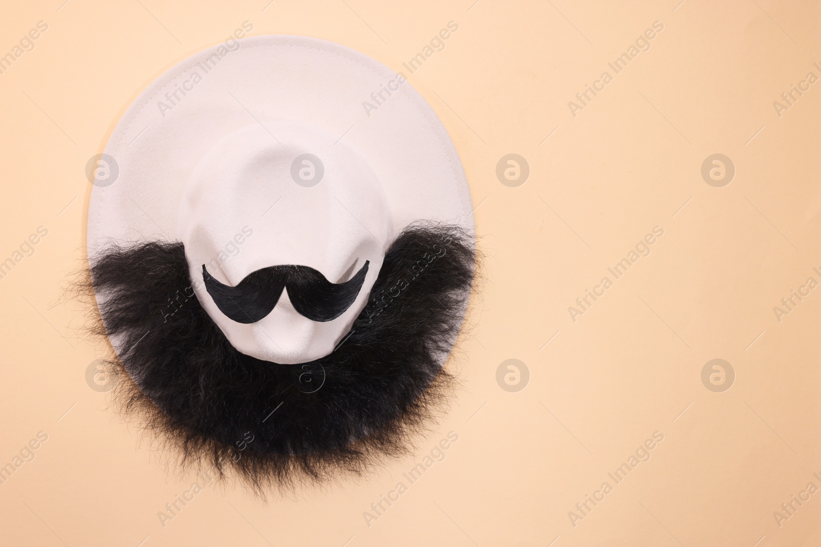 Photo of Man's face made of artificial mustache, beard and hat on beige background, top view. Space for text