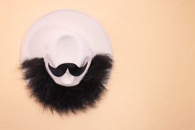 Photo of Man's face made of artificial mustache, beard and hat on beige background, top view. Space for text