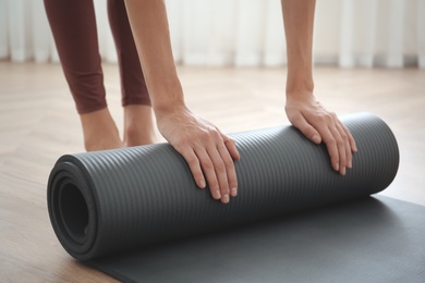 Photo of Woman rolling grey yoga mat indoors, closeup