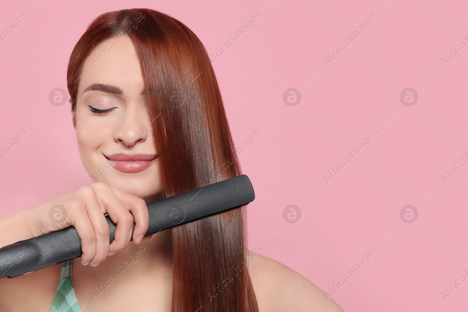 Photo of Beautiful woman using hair iron on pink background, space for text