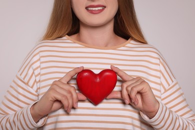 Young woman holding red heart on light grey background, closeup. Volunteer concept