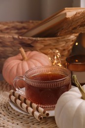 Photo of Cup of hot drink and pumpkins on wicker mat indoors