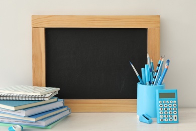 Photo of Blackboard and stationery on table near white wall, space for text. Teacher's Day