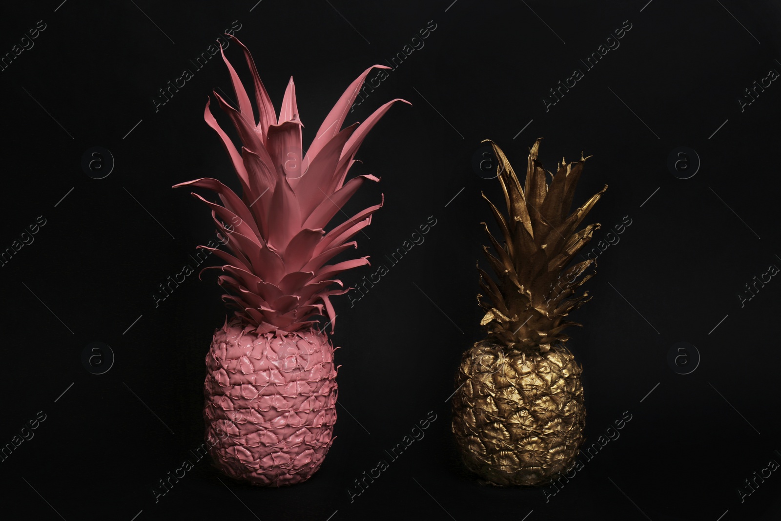 Photo of Gold and pink painted fresh pineapples on black background