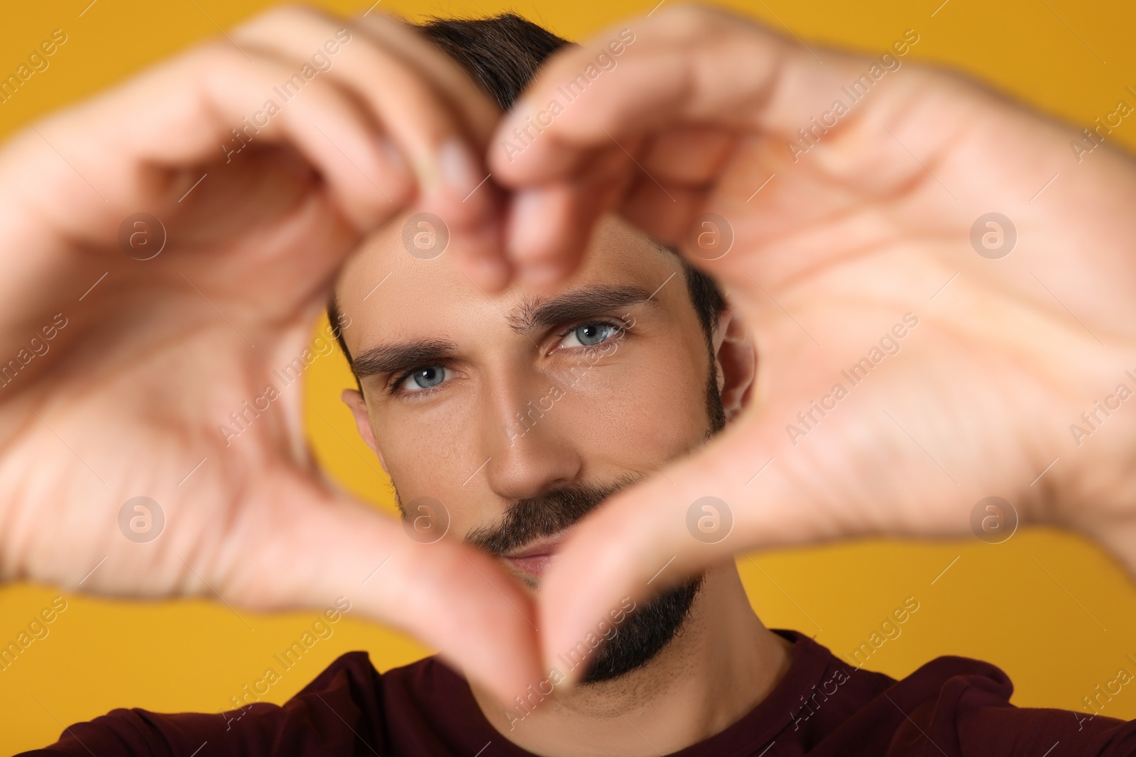 Photo of Man making heart with hands on yellow background, closeup