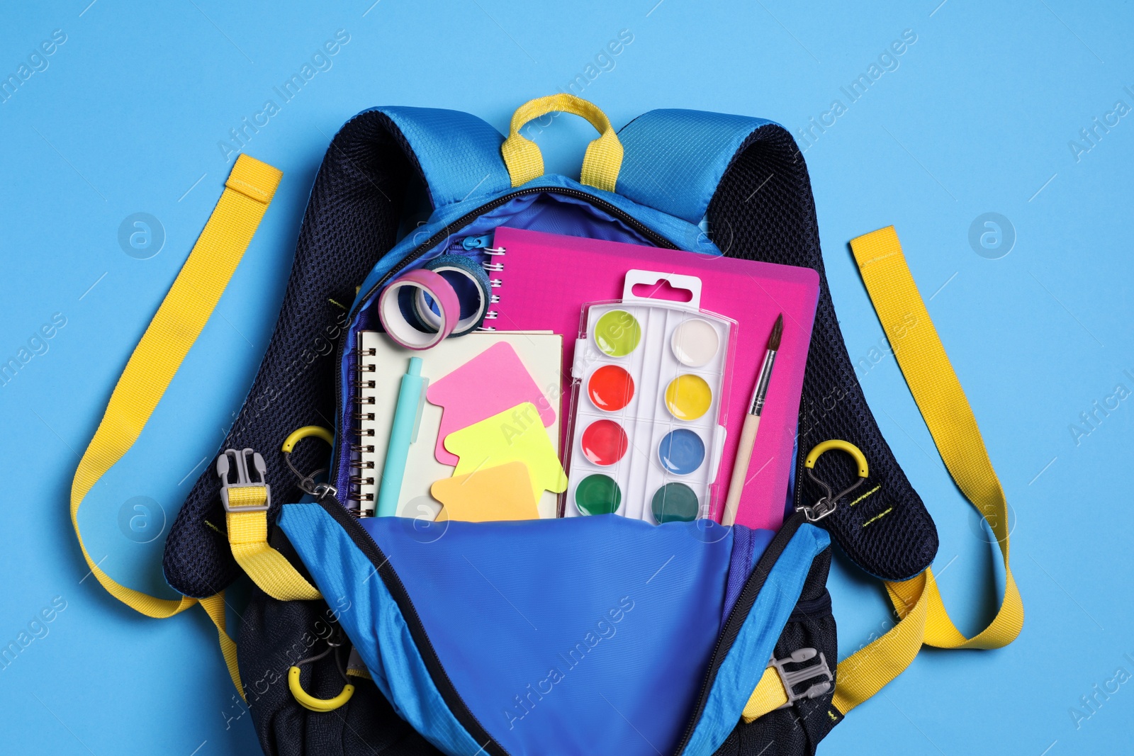 Photo of Backpack with school stationery on light blue background, top view