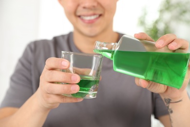 Man pouring mouthwash from bottle into glass, closeup. Teeth care