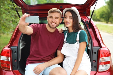 Photo of Beautiful young couple taking selfie in car trunk