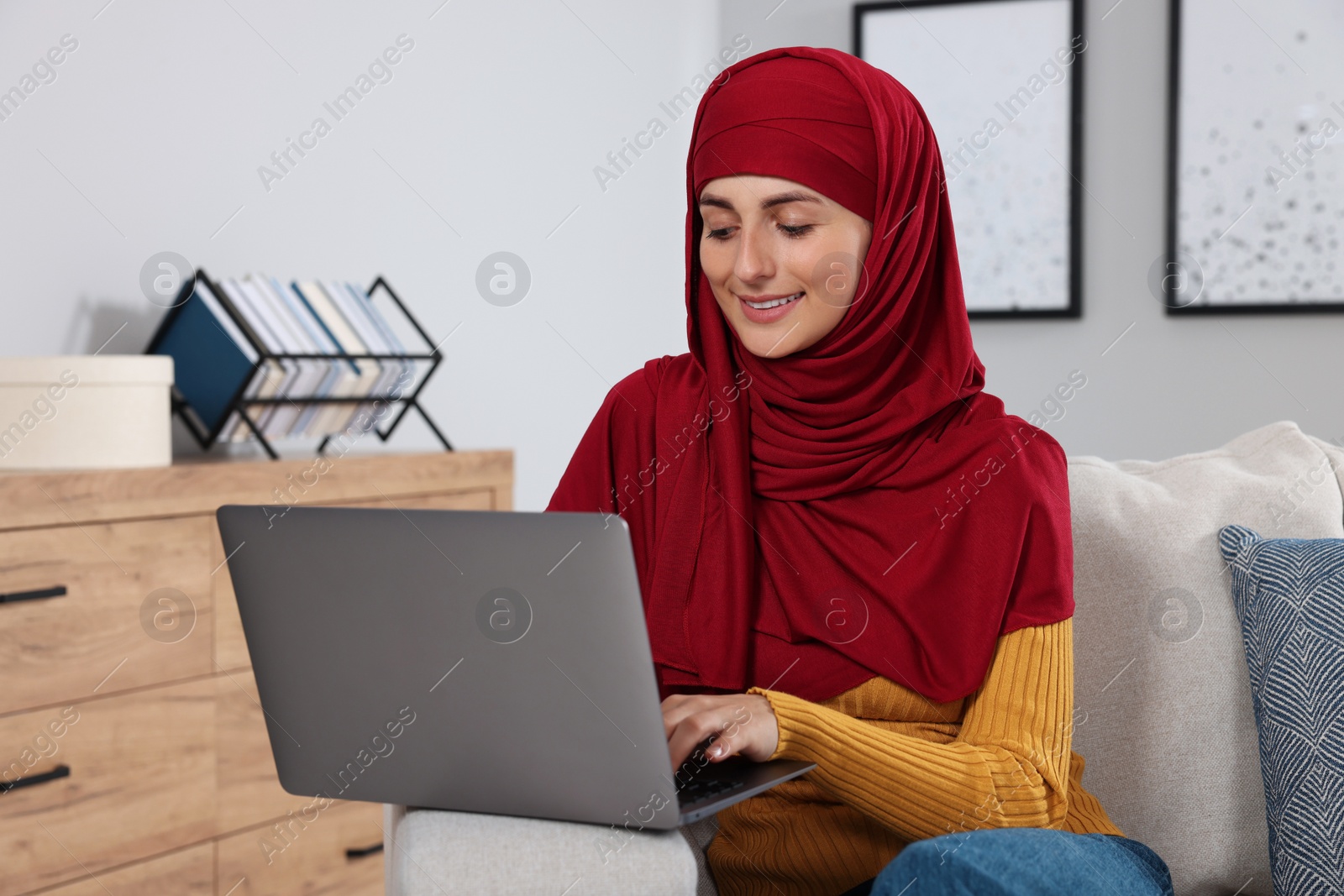 Photo of Muslim woman using laptop at couch in room